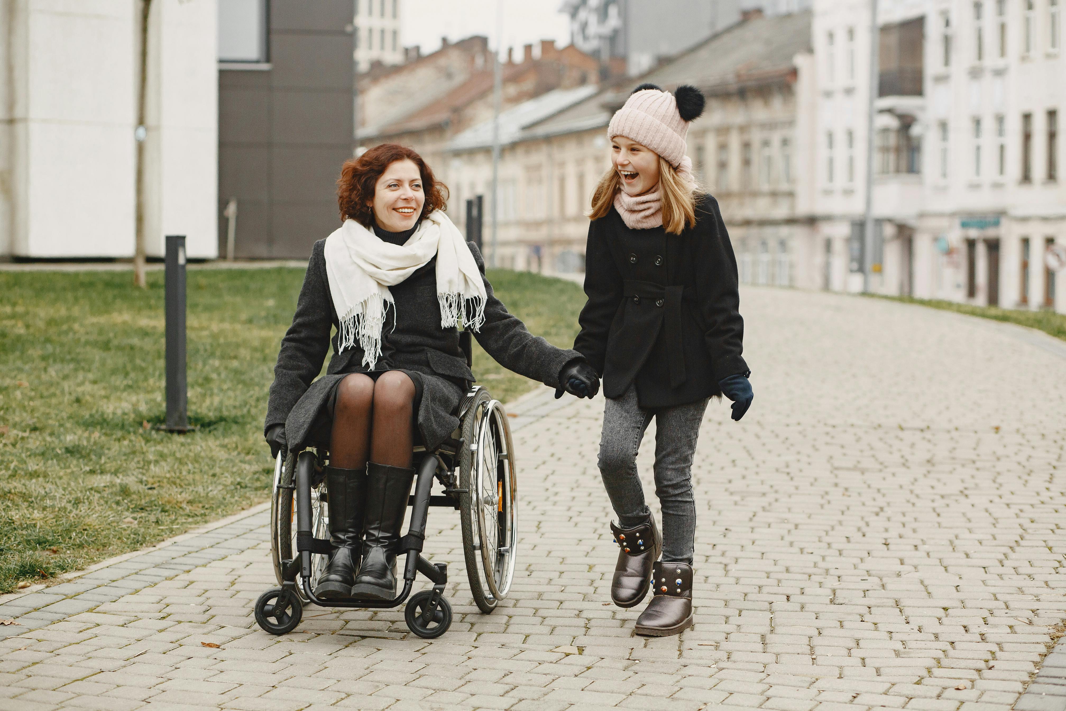 Woman in wheelchair and young girl holding hands while exploring a European city together