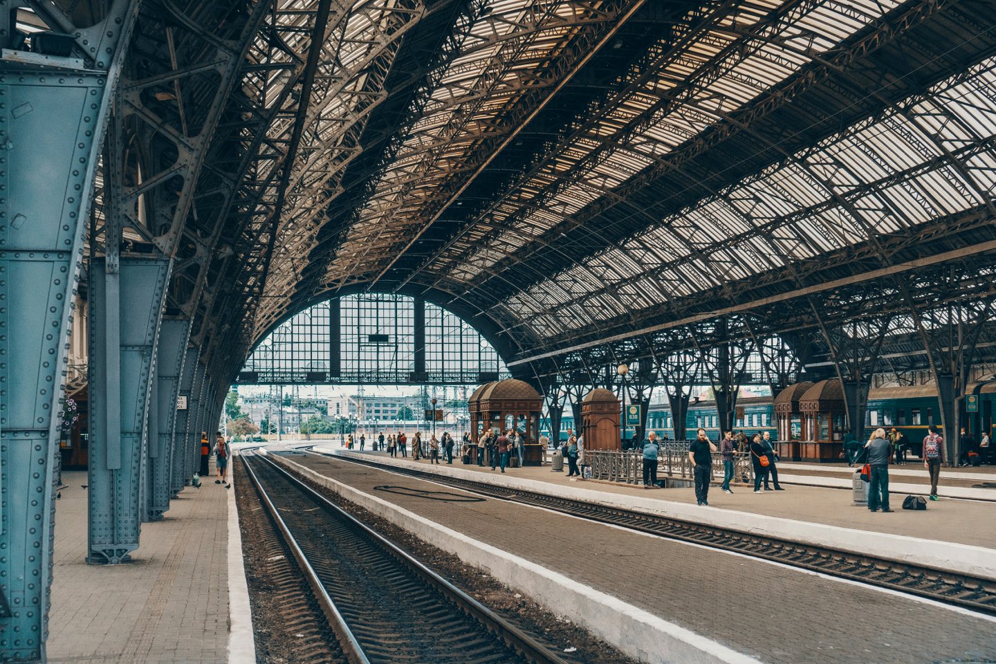 Travelers waiting on the platform of a grand historic railway station with a vaulted iron-and-glass roof